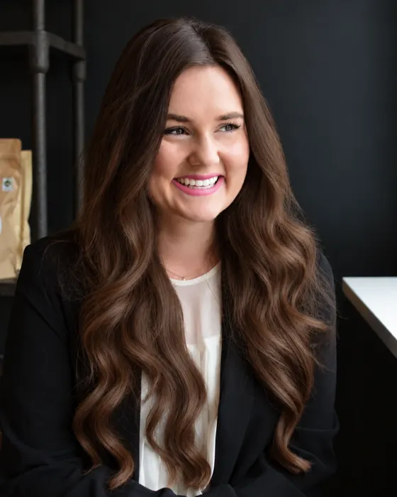 Annie Tam, smiling and looking toward a window, in a black blazer and ivory blouse